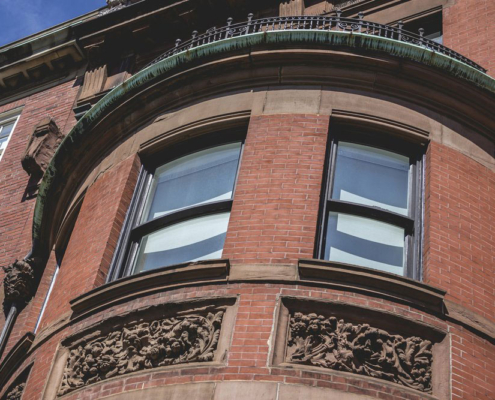 Curved bow front in brick and brownstone with tall sash windows and carved floral panels below.