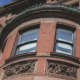 Curved bow front in brick and brownstone with tall sash windows and carved floral panels below.