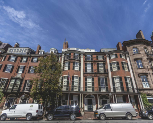 Wide brick facade with stacked bow front windows, iron balconies, and a columned portico entry.