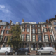 Wide brick facade with stacked bow front windows, iron balconies, and a columned portico entry.