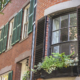 Bowed brick facade with divided-light sash, black louvered shutters open to the wall, and a window box.