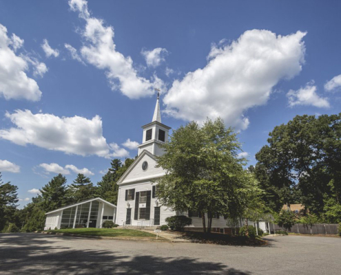 White clapboard New England church with a steeple, pedimented gable, round gable window, and shuttered sash.