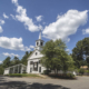 White clapboard New England church with a steeple, pedimented gable, round gable window, and shuttered sash.