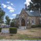 Granite Gothic Revival hall with arched wood double doors below a slate roof and turret statue.