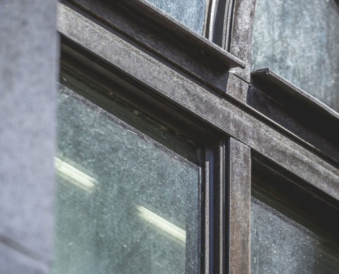 Close view of a weathered metal window frame where a vertical mullion meets a horizontal rail.