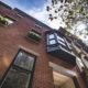 Brick rowhouse seen from below with a projecting clad oriel bay, arched sash, and window boxes.